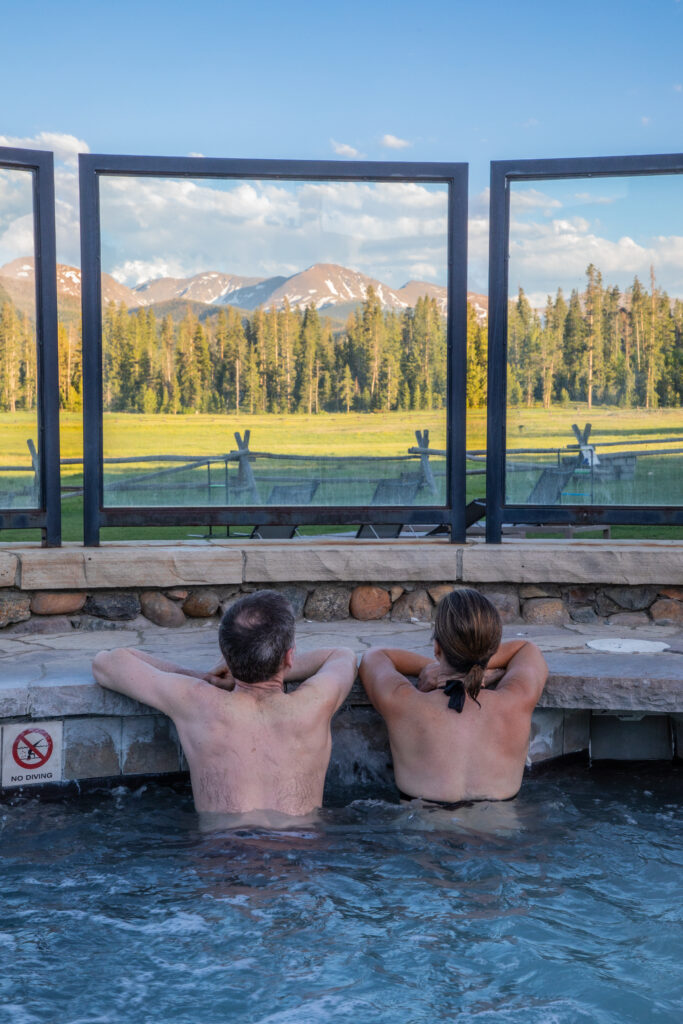 A man and woman look out at a mountain vista from a bubbling hot tub.