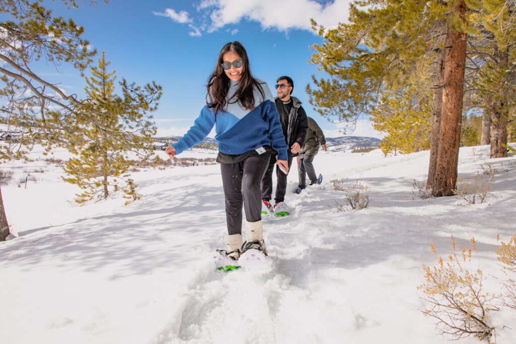 A group of smiling snowshoers walk through a snowy forest