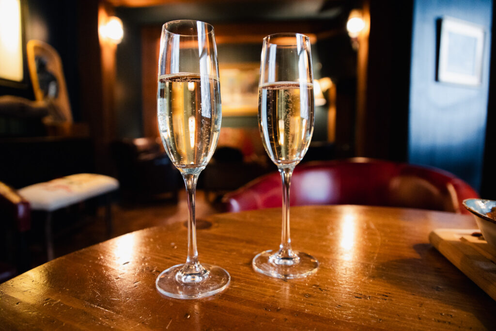 Two filled champage glasses sit on a table in a cozy room.