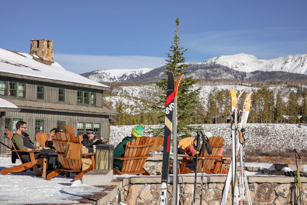 Friends relax around a fire pit with skis in the foreground